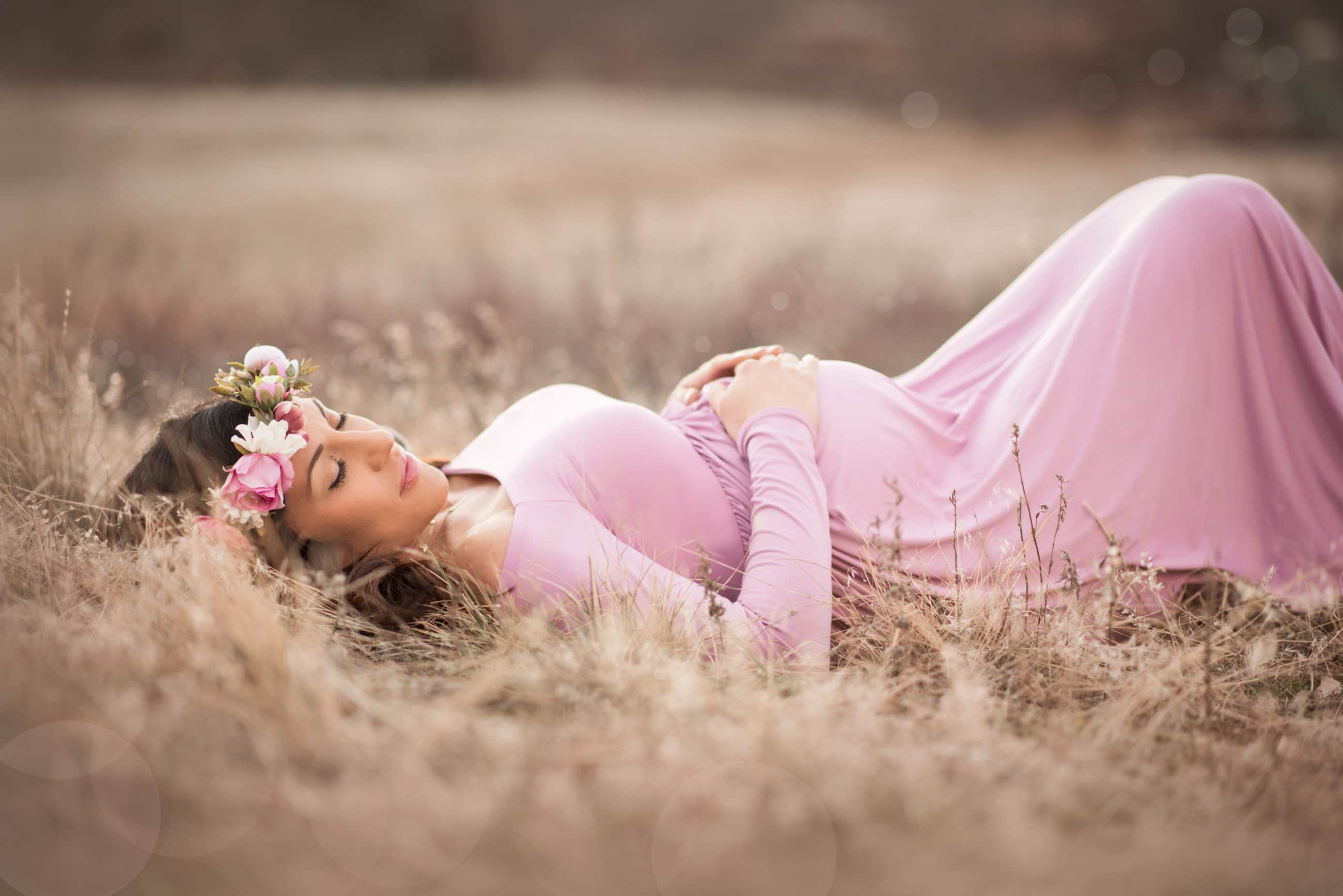 pregnant woman in pink dress laying down in golden field boulder maternity photographer