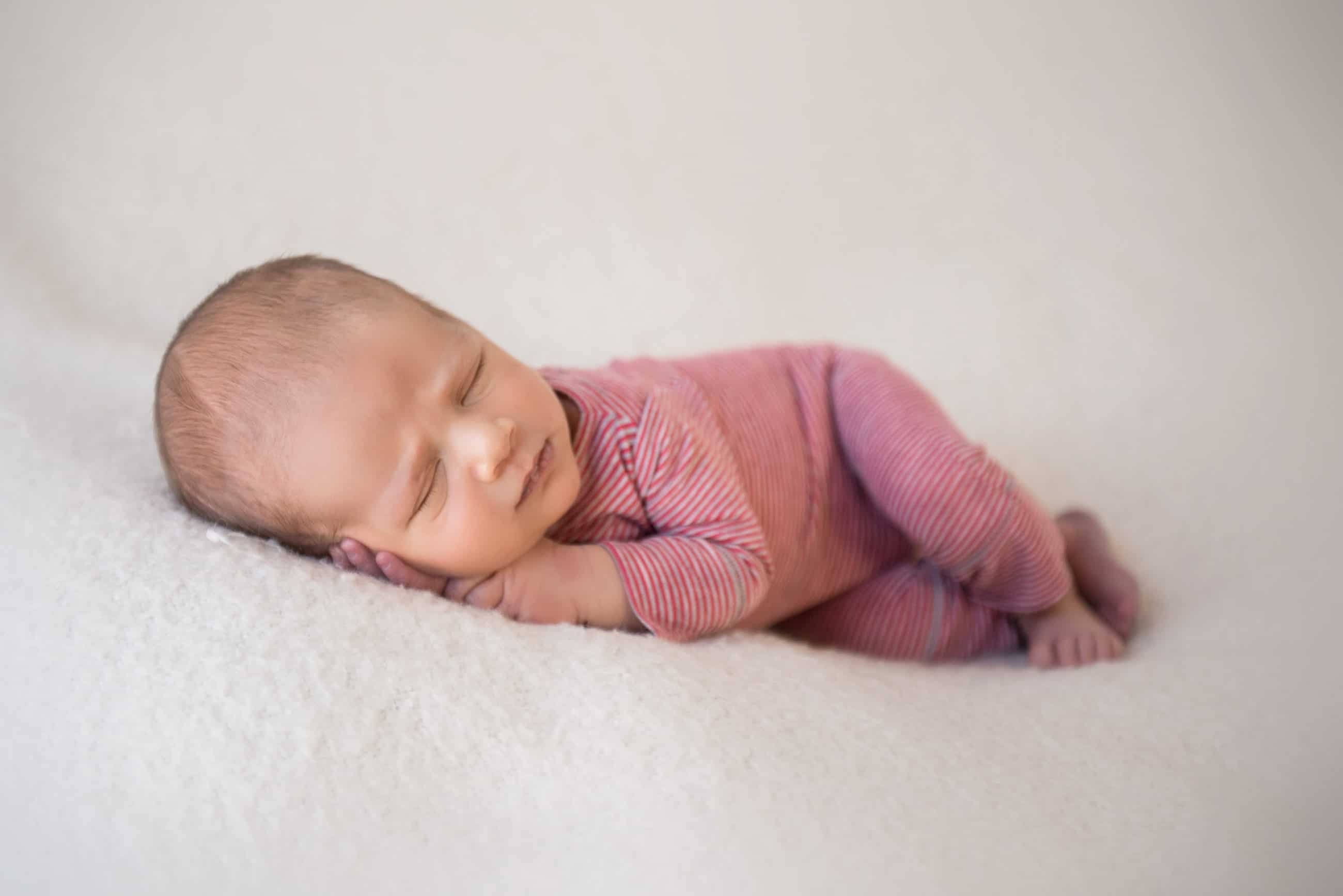 newborn baby boy in red suit sleeping on white blanket - boulder newborn photographer